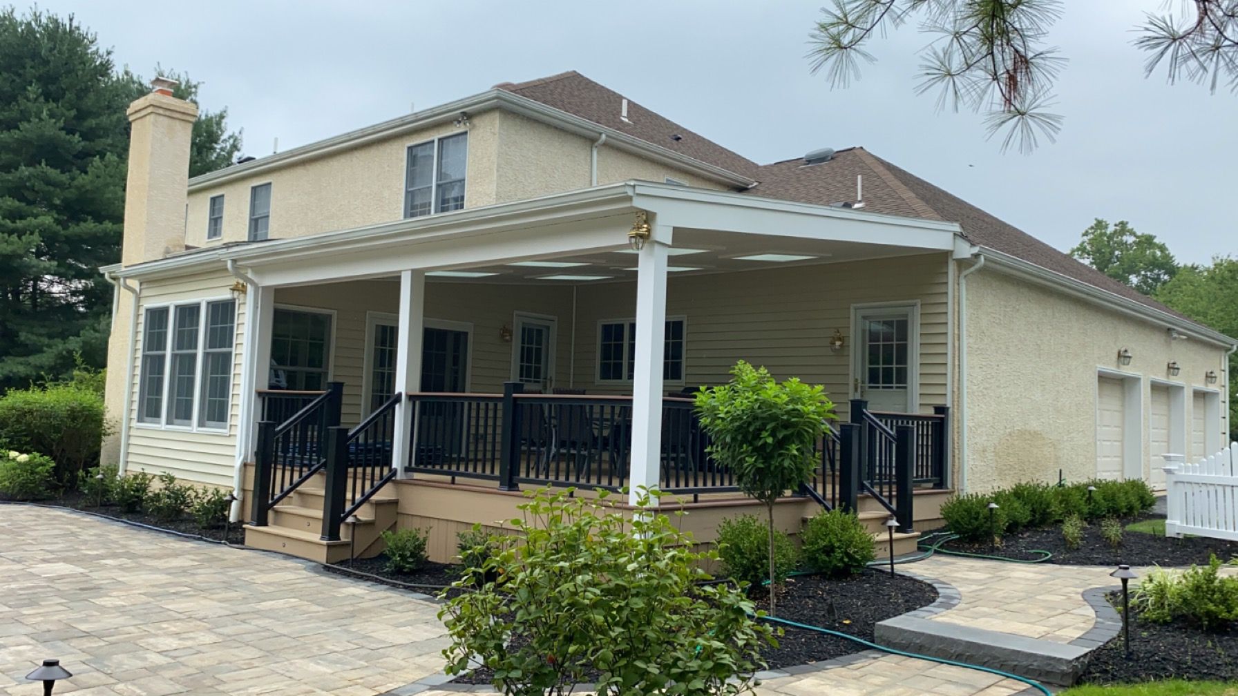 Cream-colored house with a wraparound porch, black railings, and a landscaped front yard