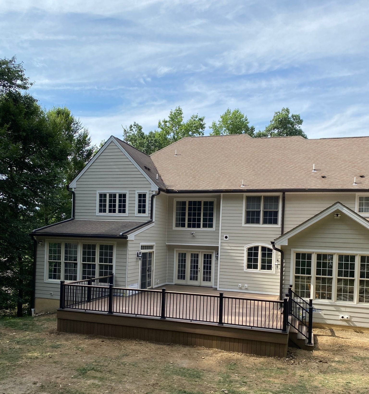 Two-story beige house with a large porch and new roof, viewed from the front yard