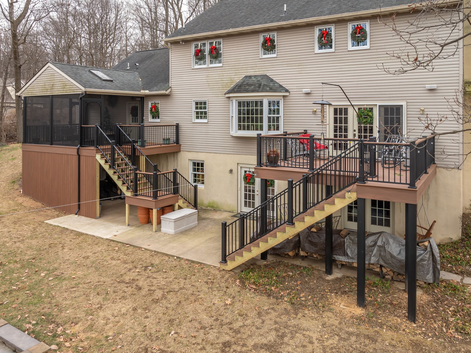 Backyard with raised deck, stairs, screened porch, and beige two-story house in winter yard