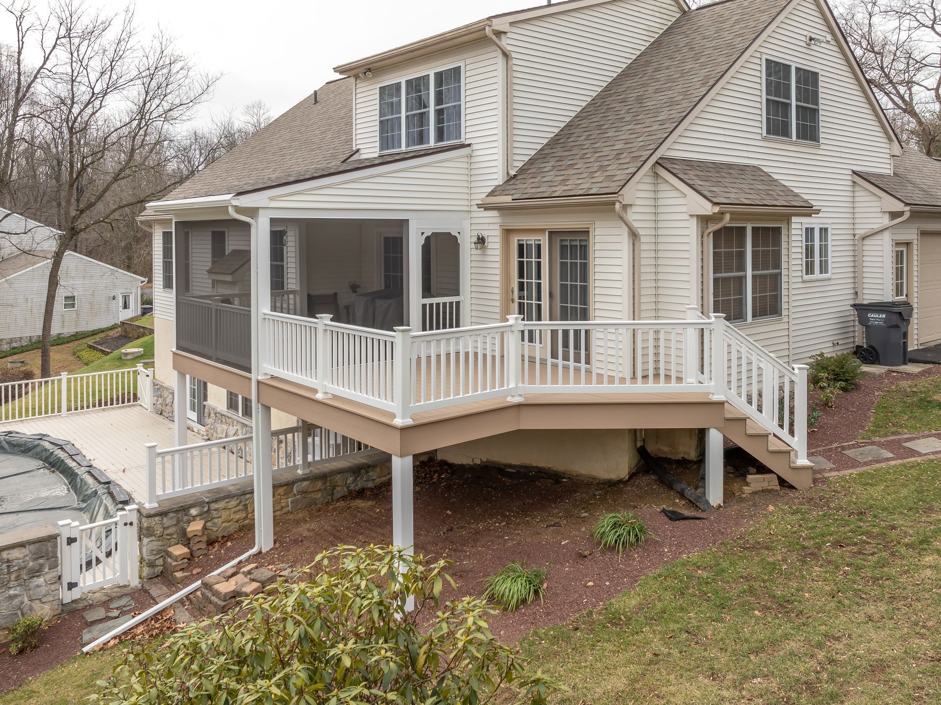 White two-story house with wraparound porch and screened-in deck on a wooded hillside