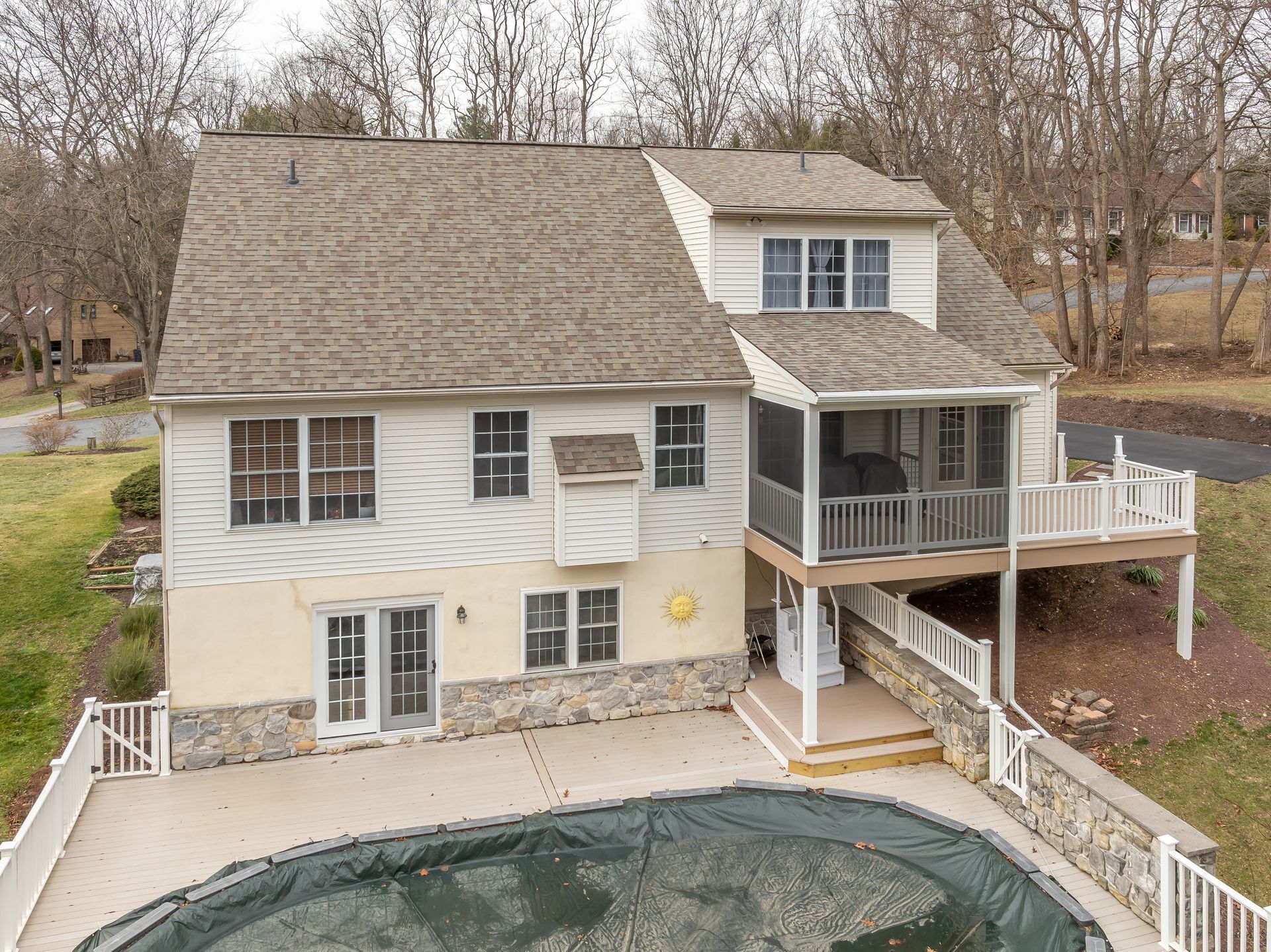 A beige two-story house with a thatched roof, deck, and in-ground pool in a wooded yard.