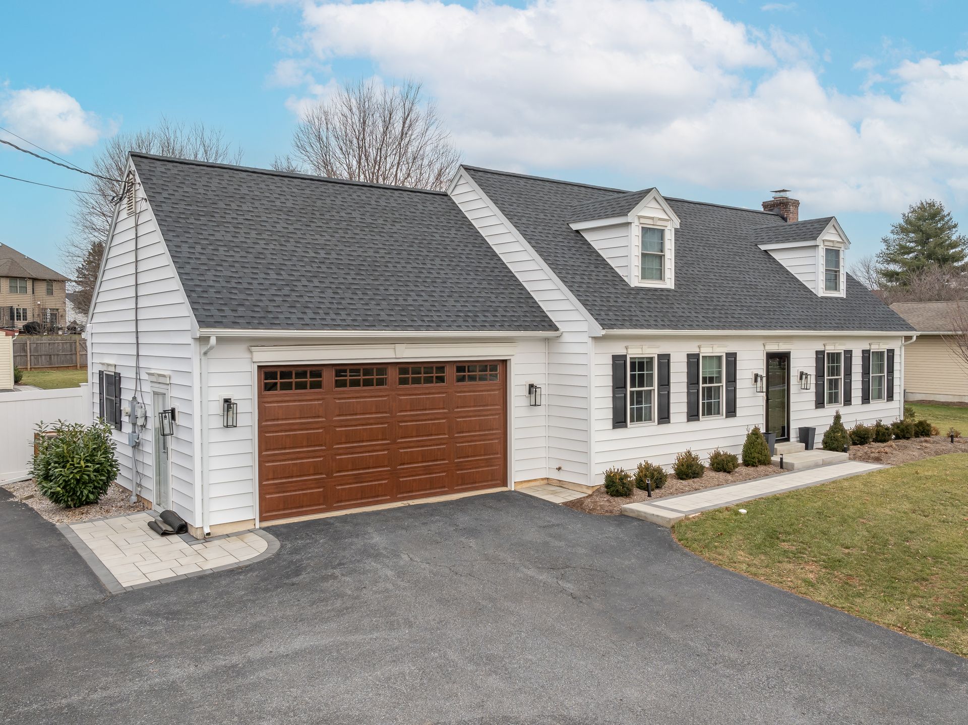 White suburban house with dark roof, brick garage, and gravel driveway