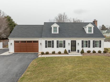 White two-story house with gray roof, black shutters, and attached wooden garage on a snowy lot