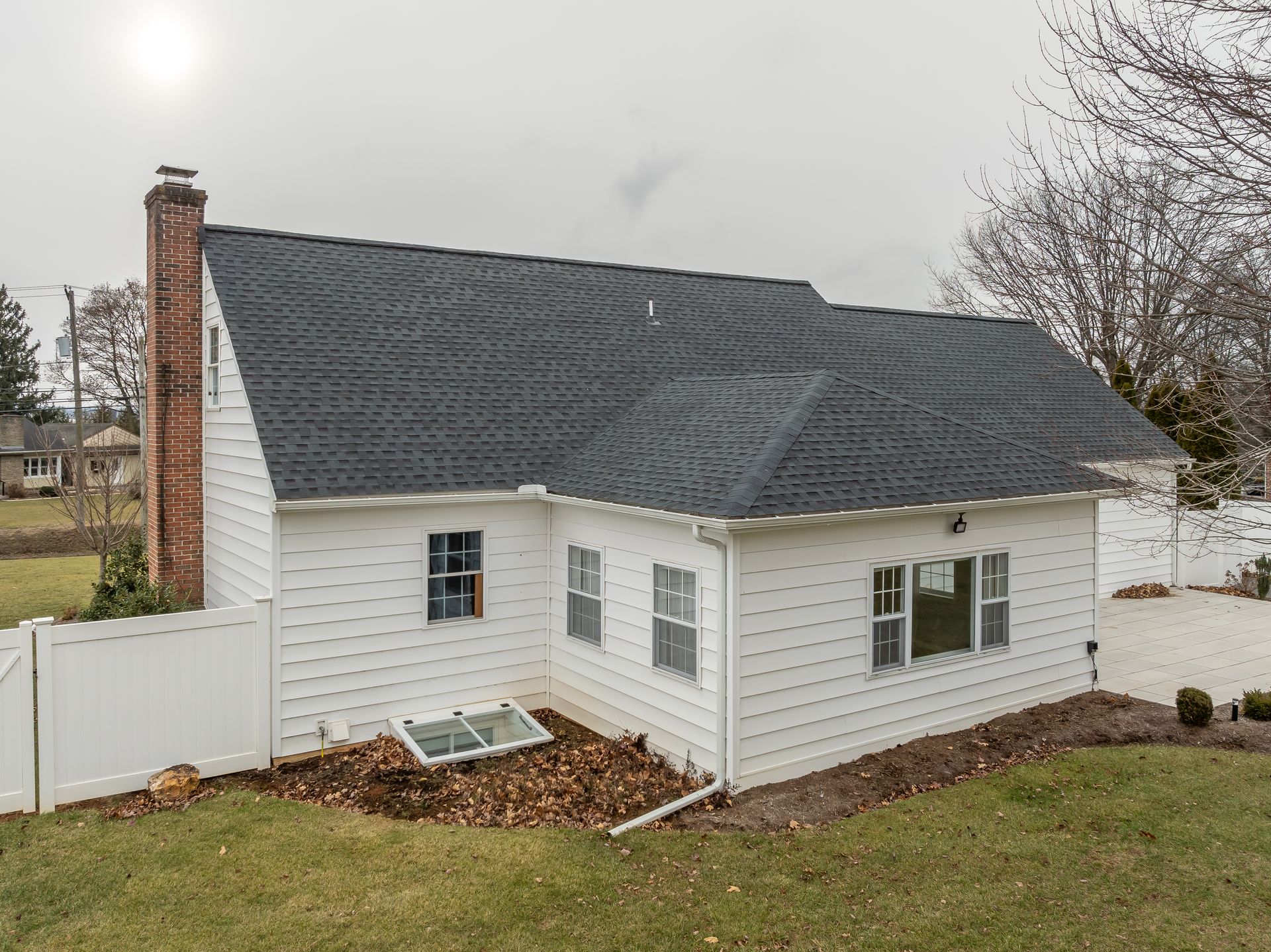 Small white house with dark roof and brick chimney in a grassy yard.
