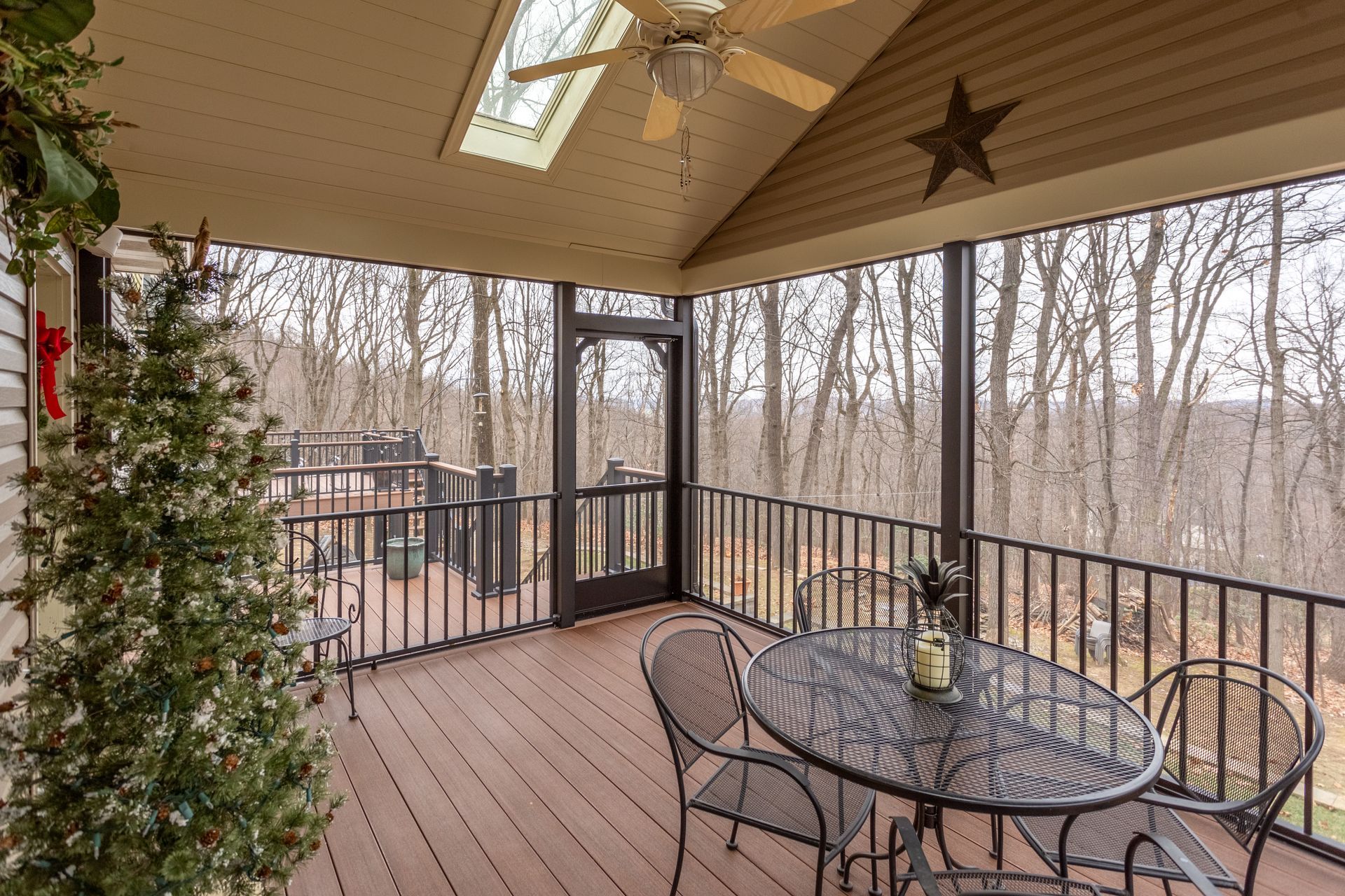 Covered wooden deck with black railing, glass table, and winter woods beyond.