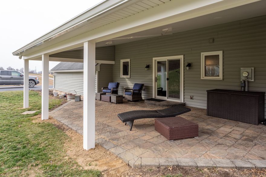 Covered patio with white posts, outdoor seating, a fire pit, and a grill outside a house.