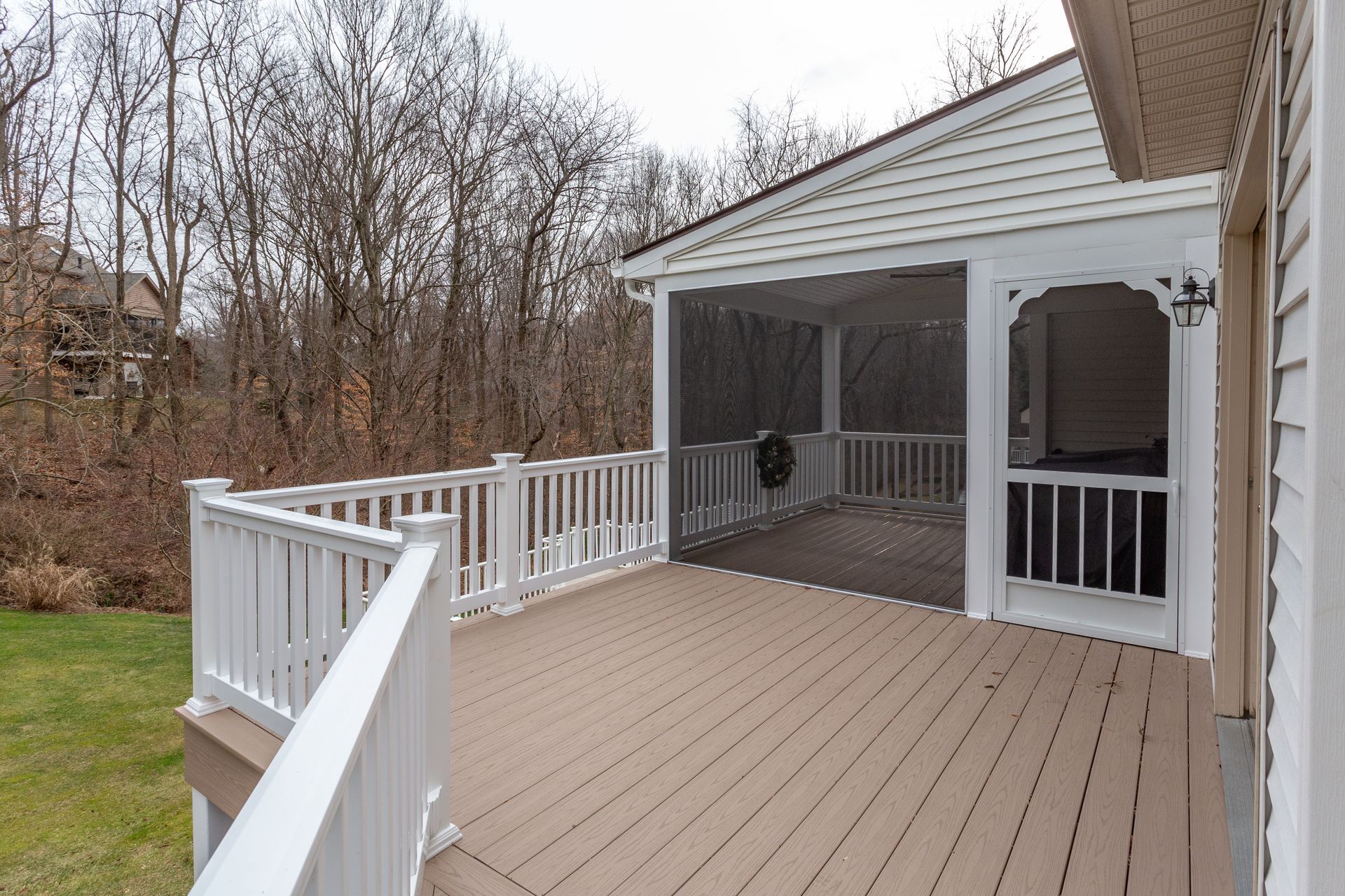 Wooden backyard deck with white railings and covered patio overlooking bare trees