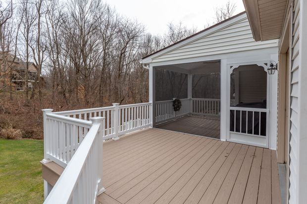 Wooden backyard deck with white railings and covered patio overlooking bare trees