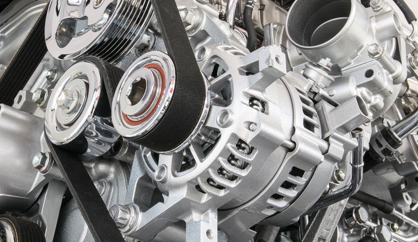Close-up of a silver engine with a black belt winding around pulleys, including an alternator.