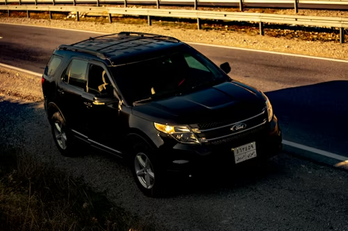 Black SUV driving on a sunlit highway beside a guardrail