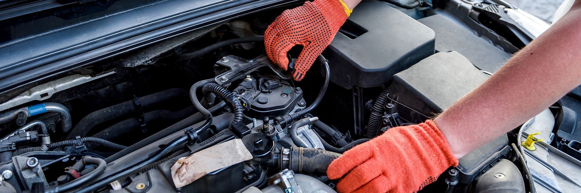 Mechanic’s gloved hands inspecting a car engine in the open hood compartment