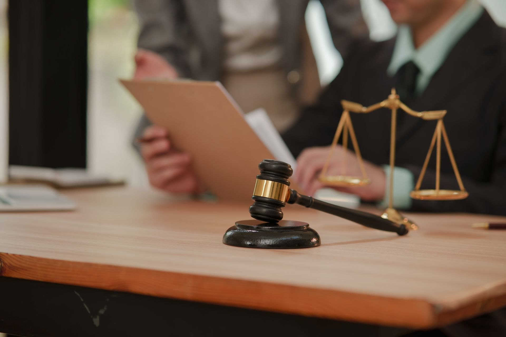 Judge’s gavel and scales of justice on a desk with legal professionals reviewing documents