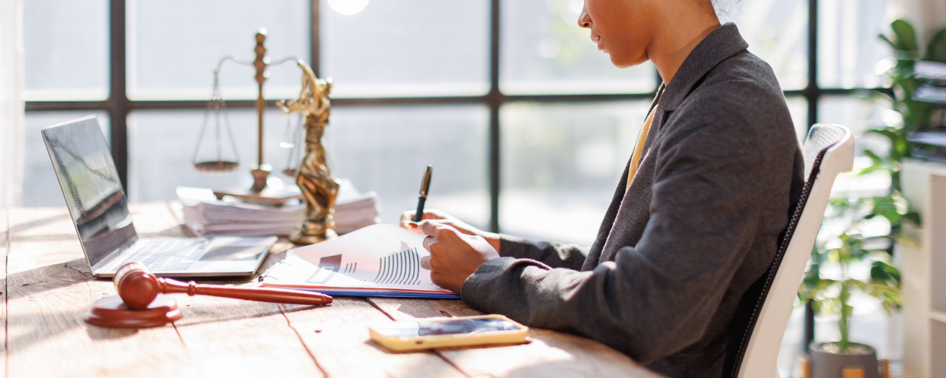 Legal professional reviewing documents at a desk with a gavel, scales of justice, and laptop nearby.
