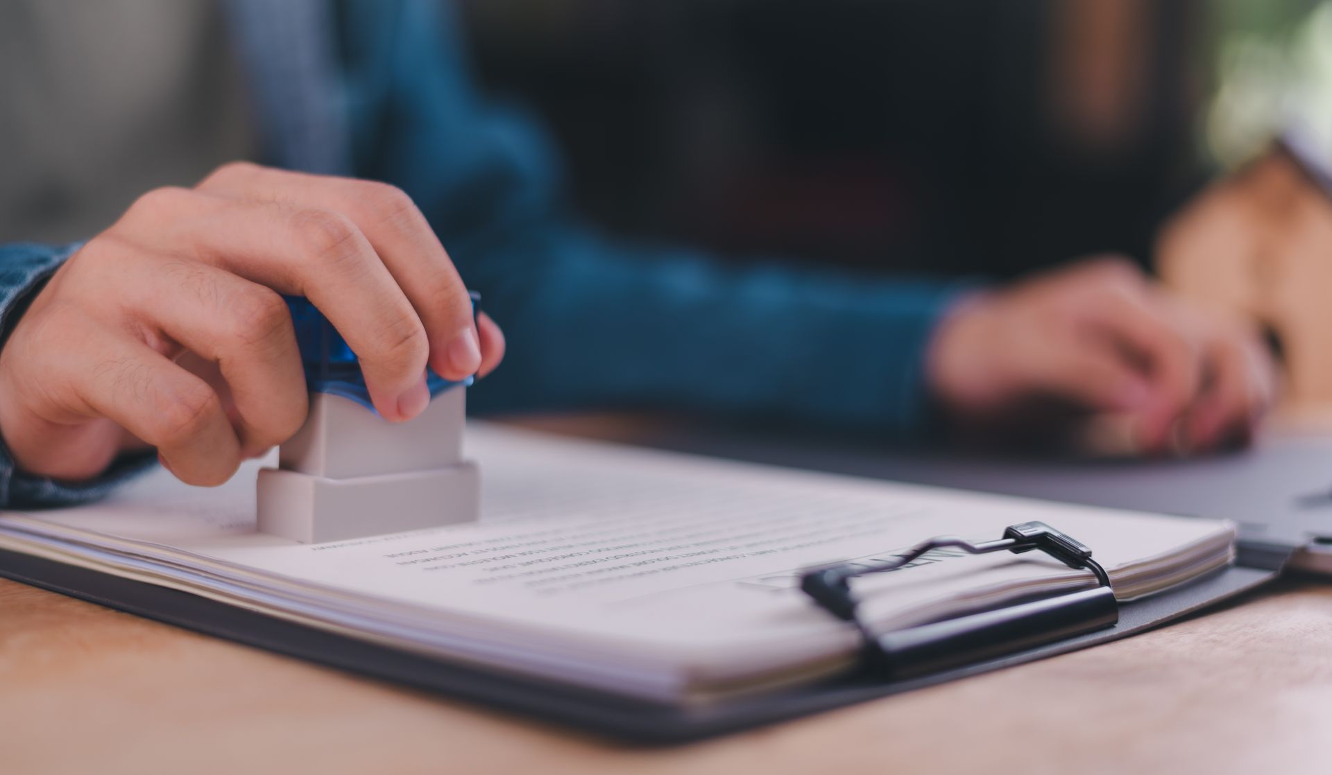 Person stamping an official document on a clipboard at a desk.]