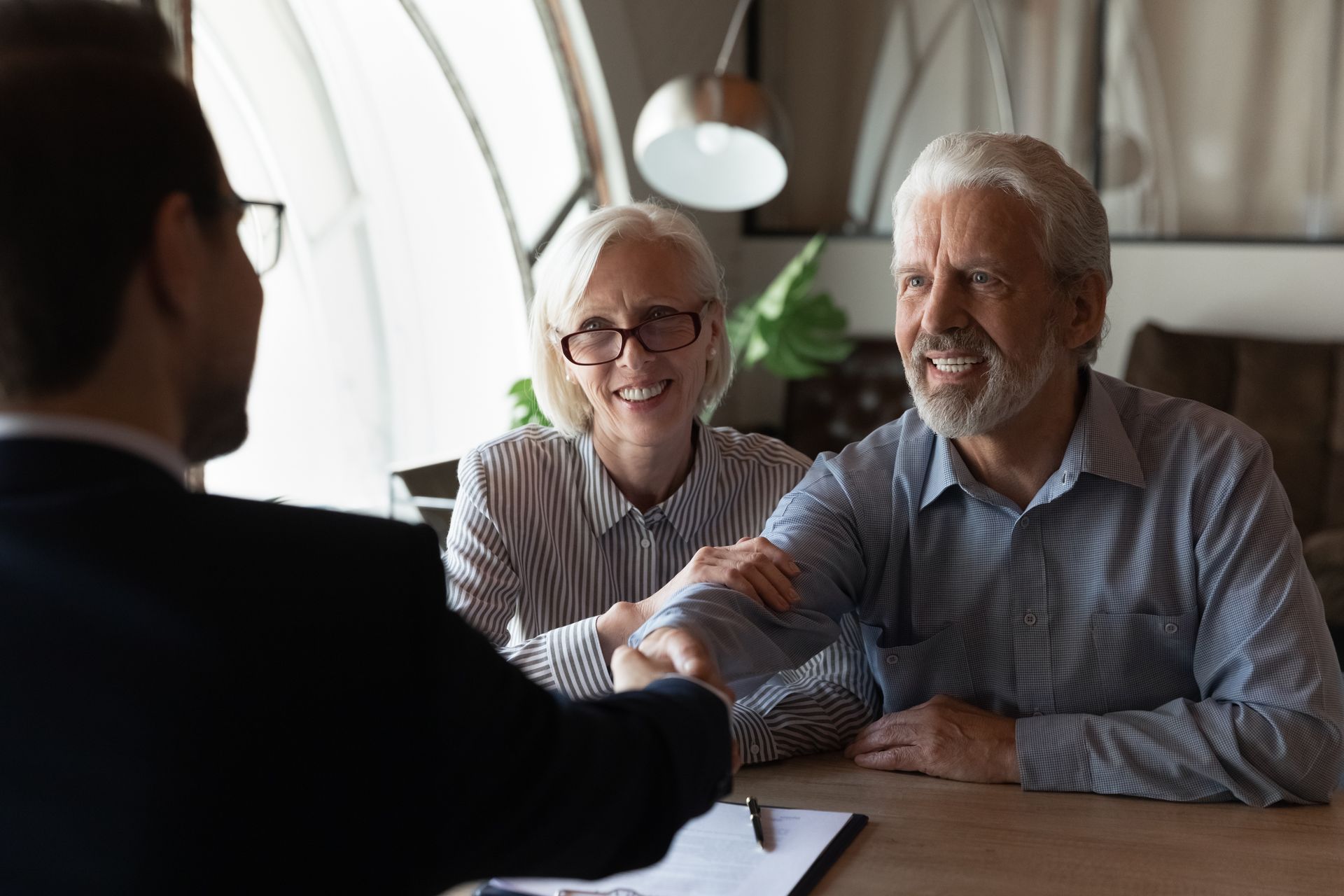 Senior couple shaking hands with advisor during meeting, discussing.