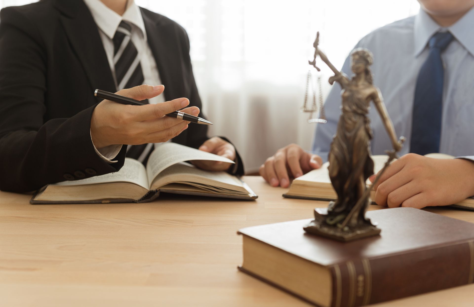 Lawyers discussing legal case with books and Lady Justice statue on office desk.