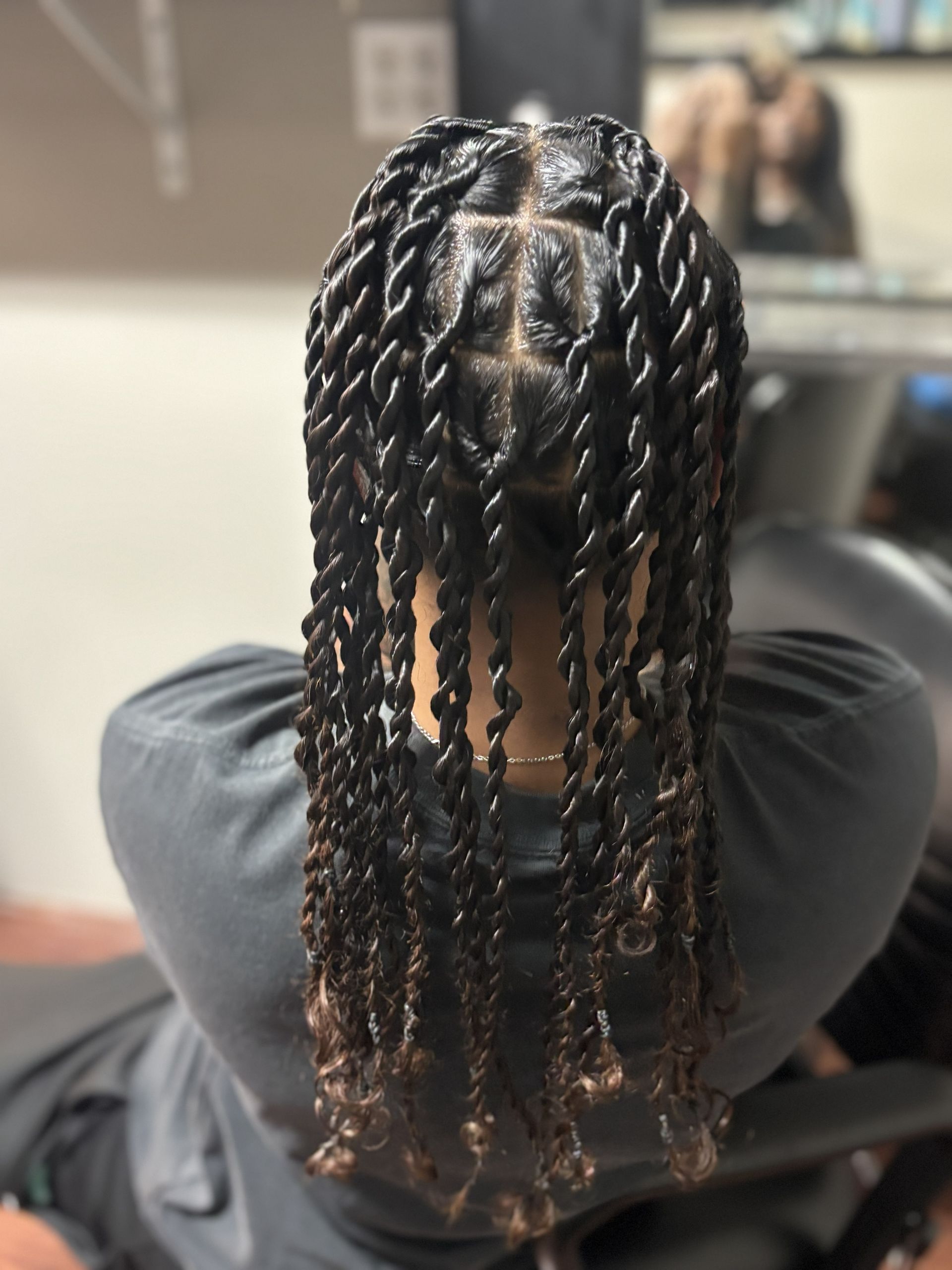 Person with braided hair seated in a salon chair, viewed from behind.