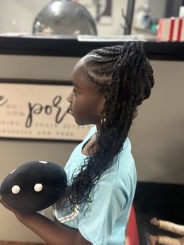 Child in profile holding a black plush toy with white eyes, standing indoors near a counter.