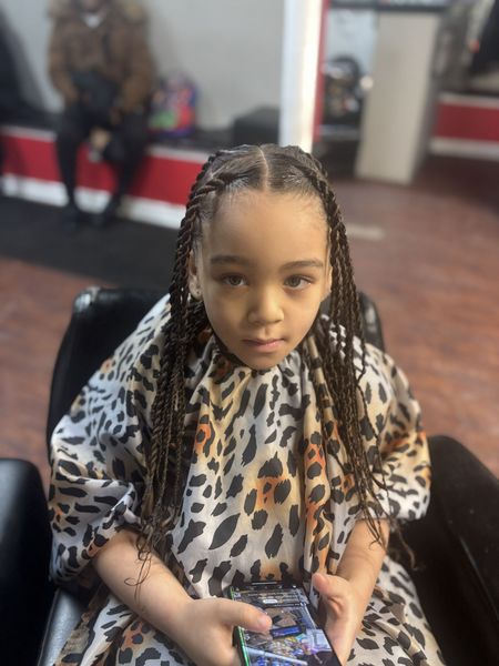 Young child in a leopard-print cape seated in a salon chair, holding a phone and looking at the camera.