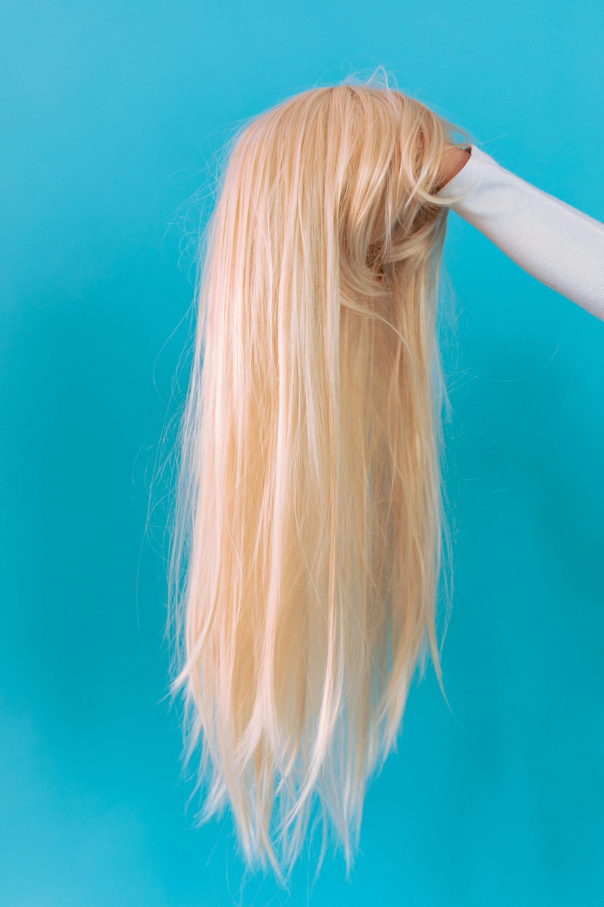 Blonde hair extensions held against a turquoise background