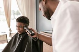 Barber trimming a client’s hair with clippers in a bright salon