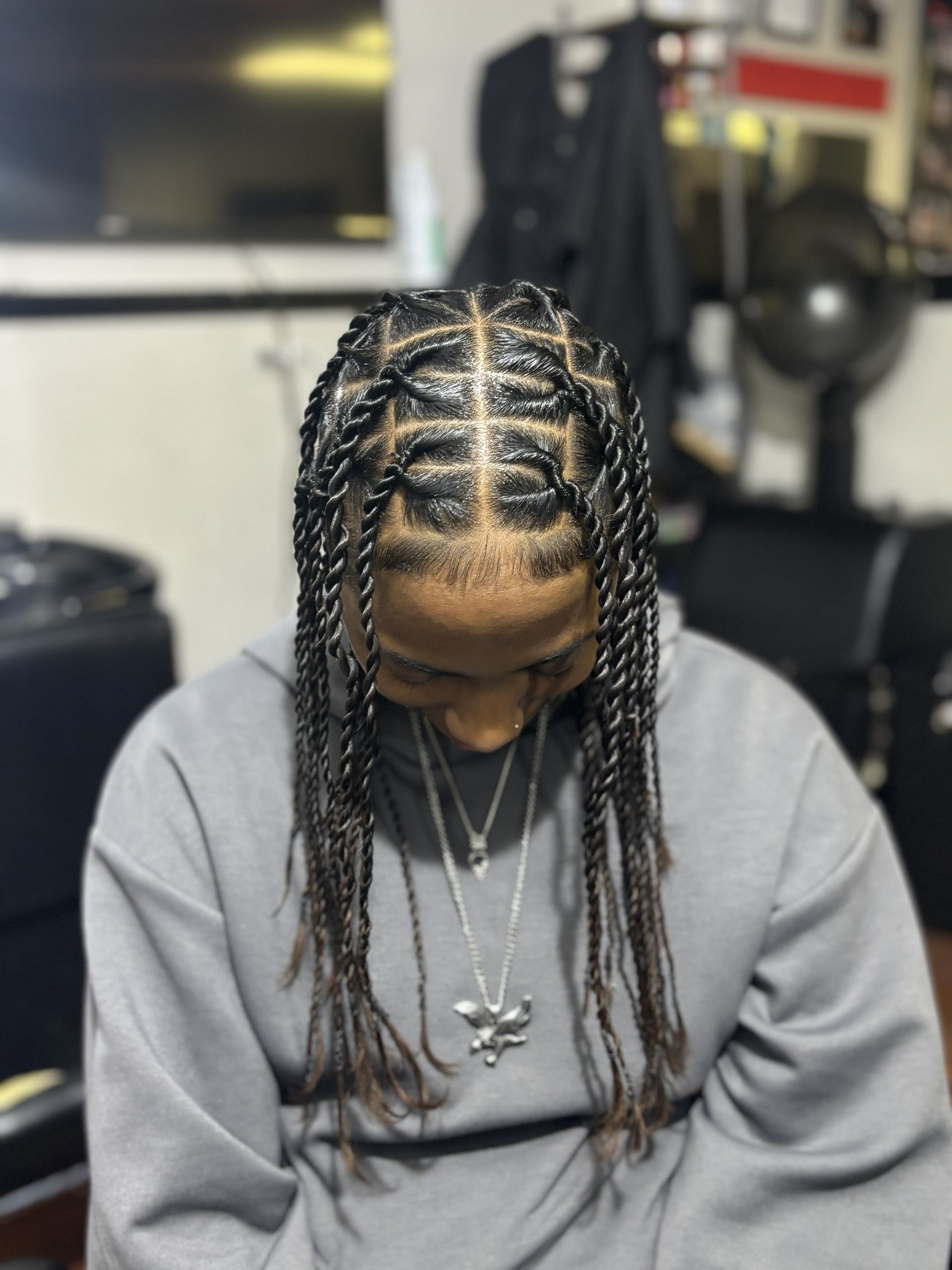 Person with braided hair looking down, wearing a gray sweatshirt in an indoor setting