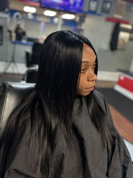 Person with long straight black hair sitting in a salon chair, looking to the side.