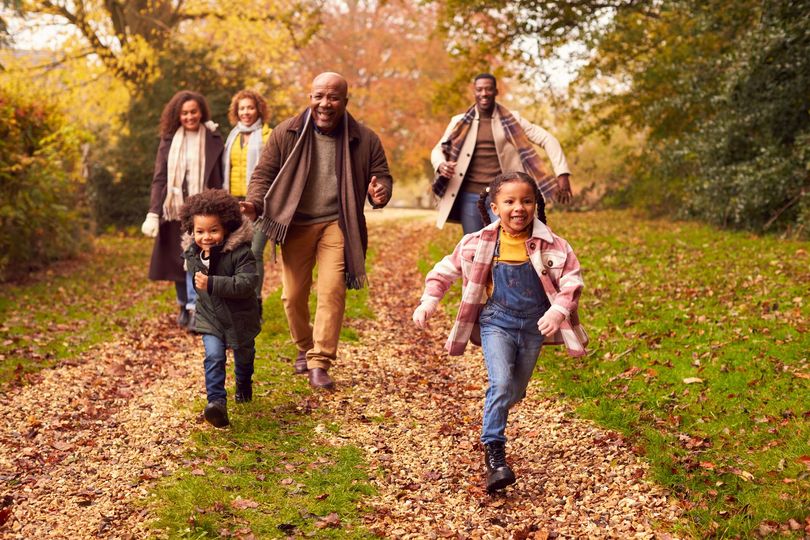 Family walking together on a leaf-covered path in autumn, smiling and carrying backpacks