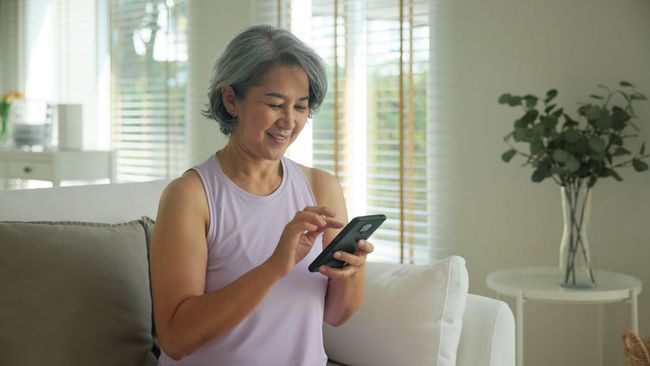 Person smiling while using a smartphone on a couch in a bright living room