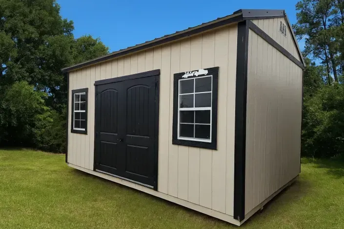 Small beige storage shed with black double doors and white-trimmed windows on a grassy lawn.