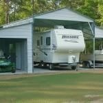 White camper trailer parked under a metal carport in a grassy yard