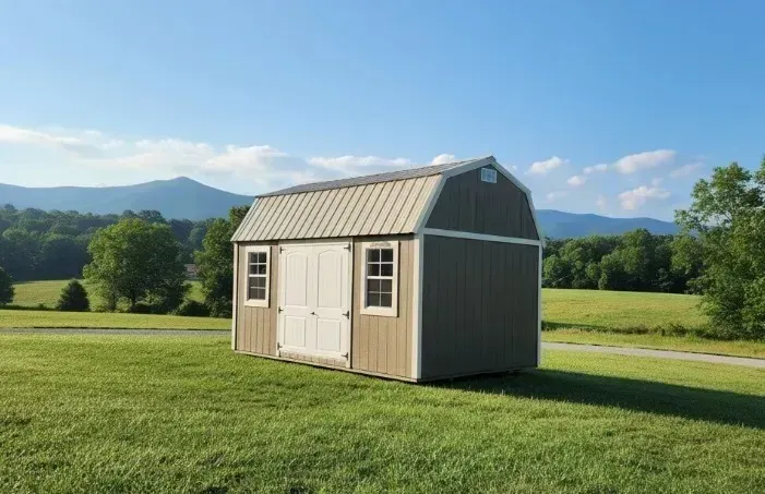 Small beige shed in a grassy field with mountains and blue sky in the background
