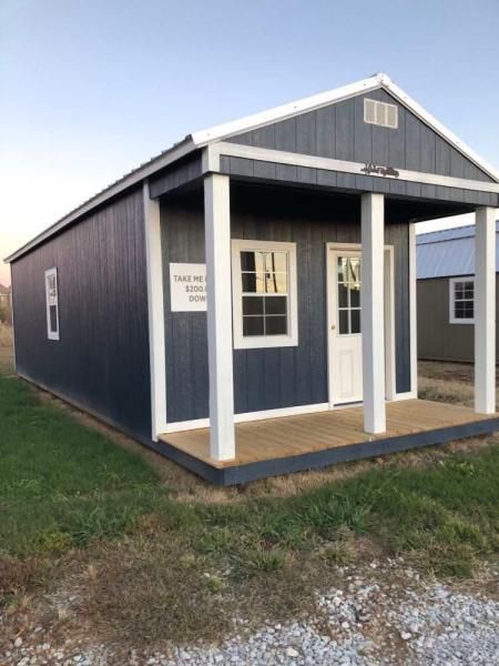 Small dark blue shed with white trim, porch, and double doors on a grassy lot.