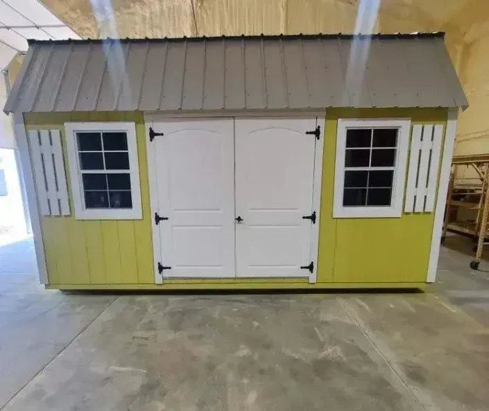 Small yellow-and-white shed with gray roof and double doors, shown indoors on a concrete floor