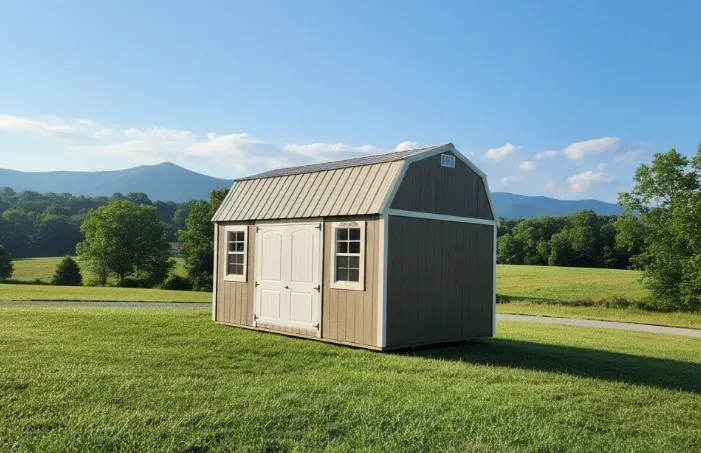 Small beige shed with white doors in a sunny green field, mountains in the background