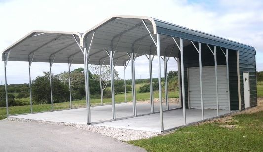 Covered metal carport on a concrete pad beside a grassy field, with two open bays and a storage room.