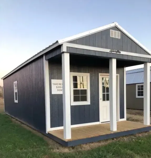 Small navy-blue house with white trim and porch on a grassy lot under a clear sky