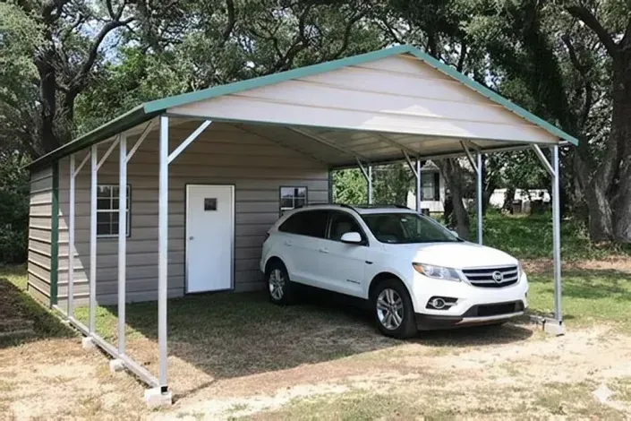 Silver SUV parked under a white metal carport beside a small shed in a wooded yard