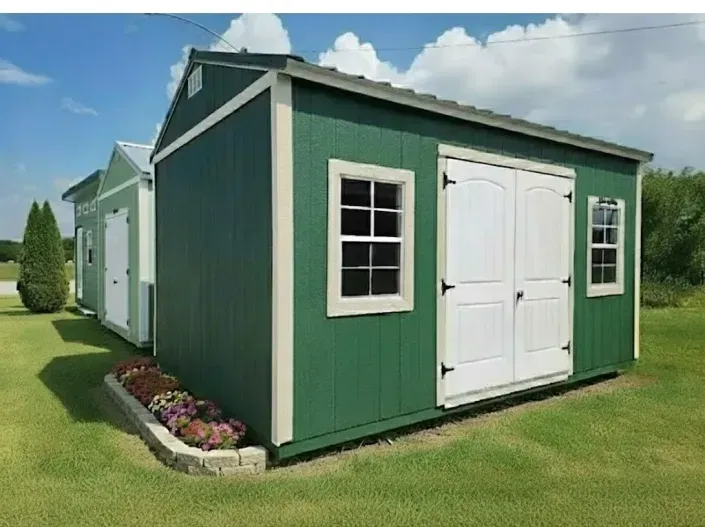 Green backyard shed with white double doors and windows on a grassy lawn