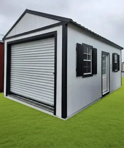 White portable garage or storage shed with roll-up door, black trim, and side window on green grass