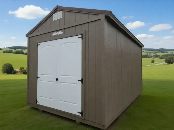 Small gray shed with white double doors on a grassy field under a blue sky.