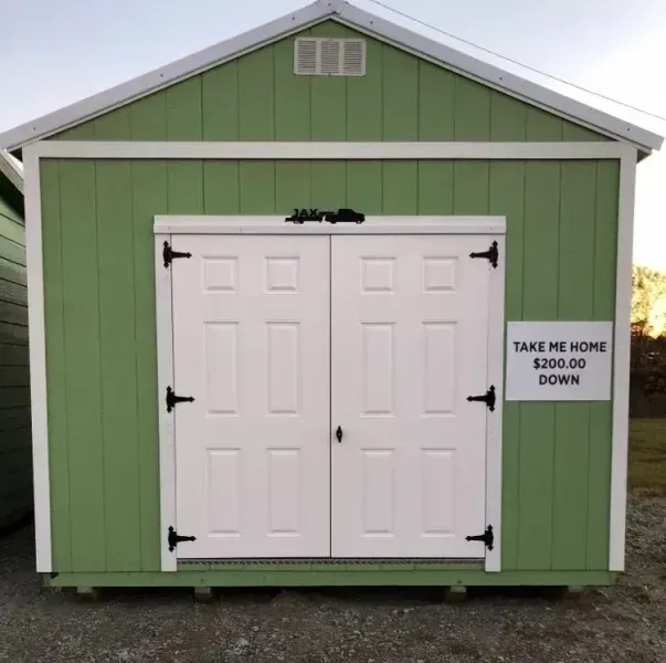 Green backyard shed with white double doors and a sign reading “Take me home $200 down”