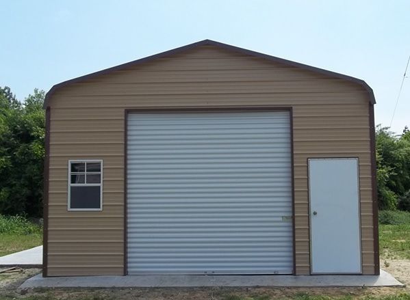 Tan metal storage shed with roll-up garage door, side entry door, and small window on a concrete pad