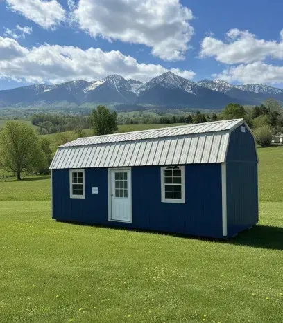 Blue shed on a green lawn with snowy mountains and clouds in the background