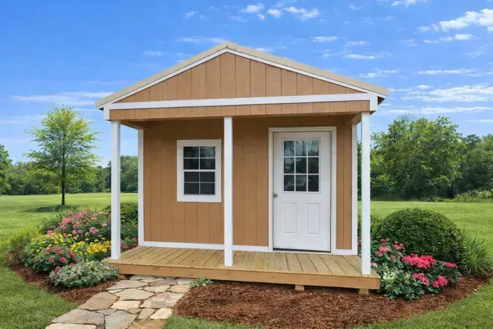 Small tan garden shed with white trim and door, framed by flowers and grass under a blue sky.