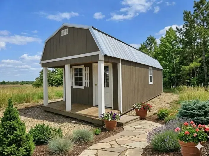 Small brown cabin with metal roof and porch, set among flowers and a stone garden path under a blue sky