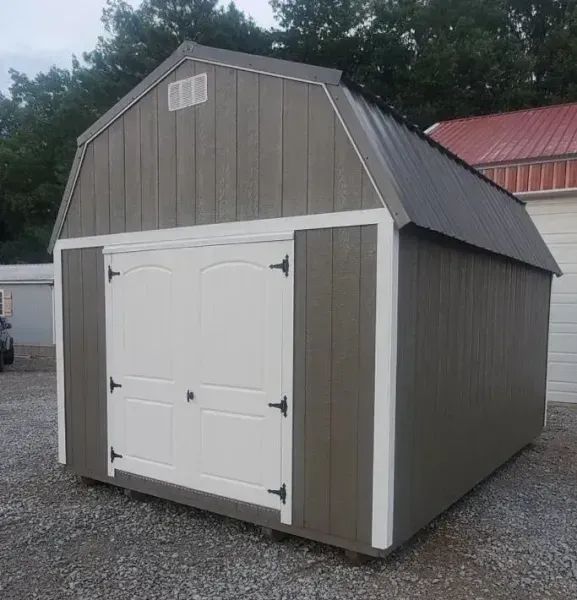 Gray barn-style shed with white double doors on a gravel lot