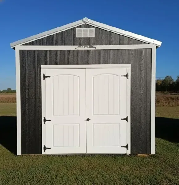 Gray barn shed with white double doors and trim, standing on grass under a blue sky.