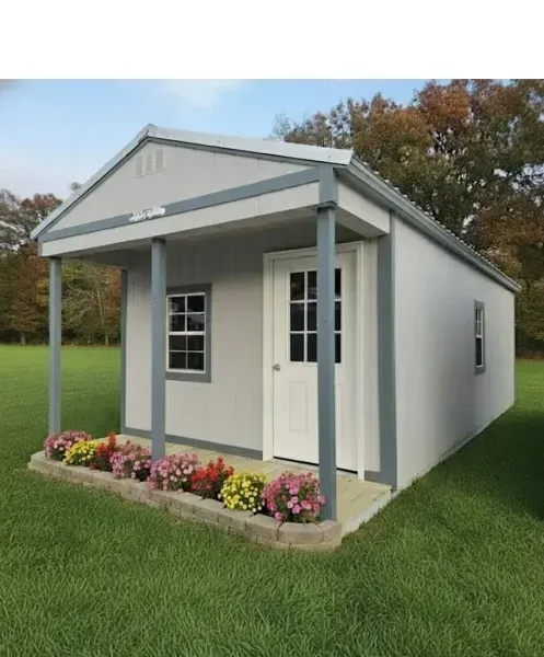 Small white cottage with gray porch, flower bed, and green lawn outdoors