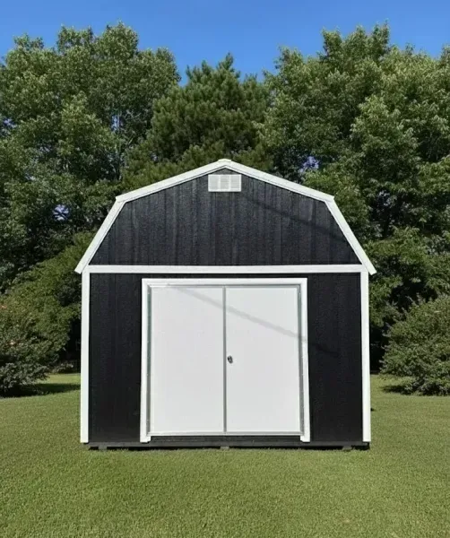 Black barn-style shed with white trim and double doors on a grassy lawn under trees